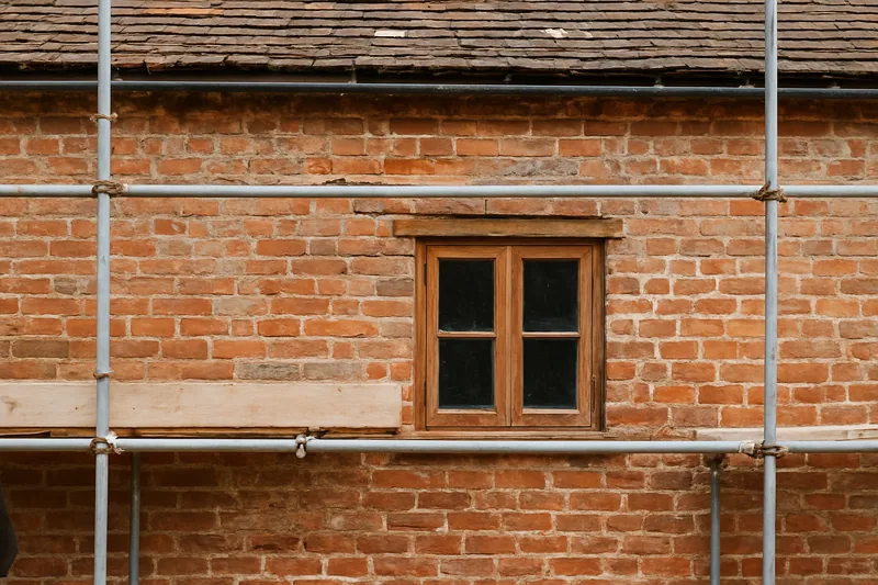 A single-storey old brick cottage wall with a timber window, partly scaffolded — heritage repointing, Ballarat. Illustrative example.